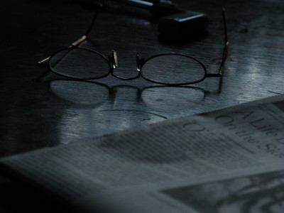 Fishkill. April, 2009. reading glasses and newspaper on shiny cherry wood table surface.